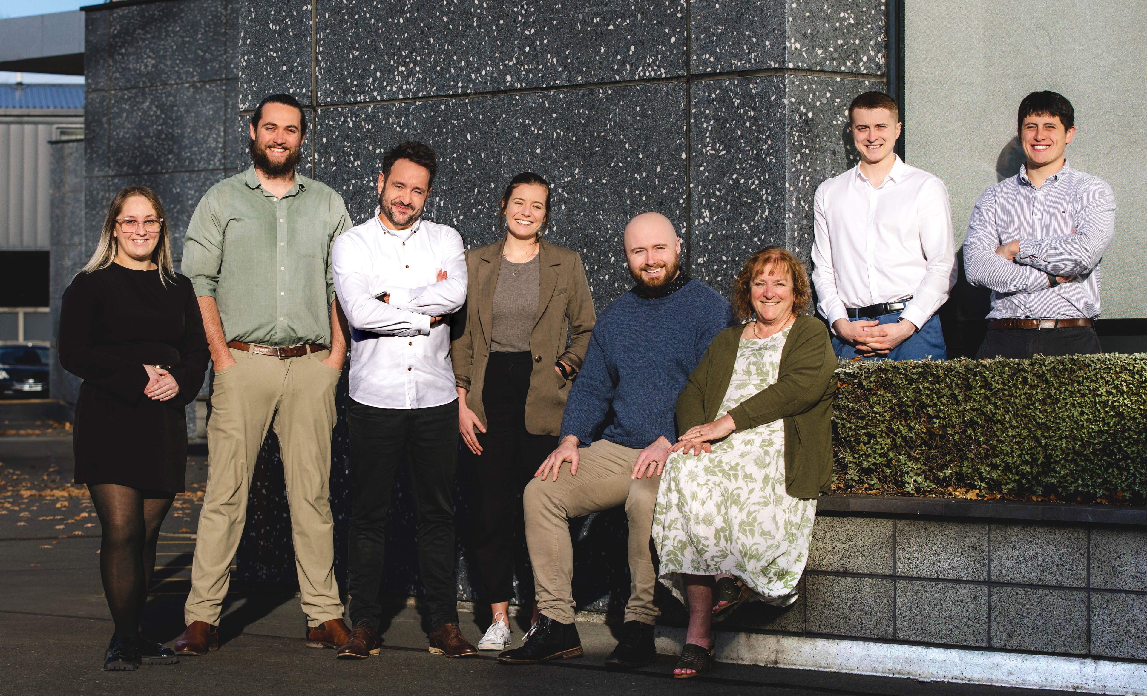 Group of people posing together in front of a building with a textured wall.